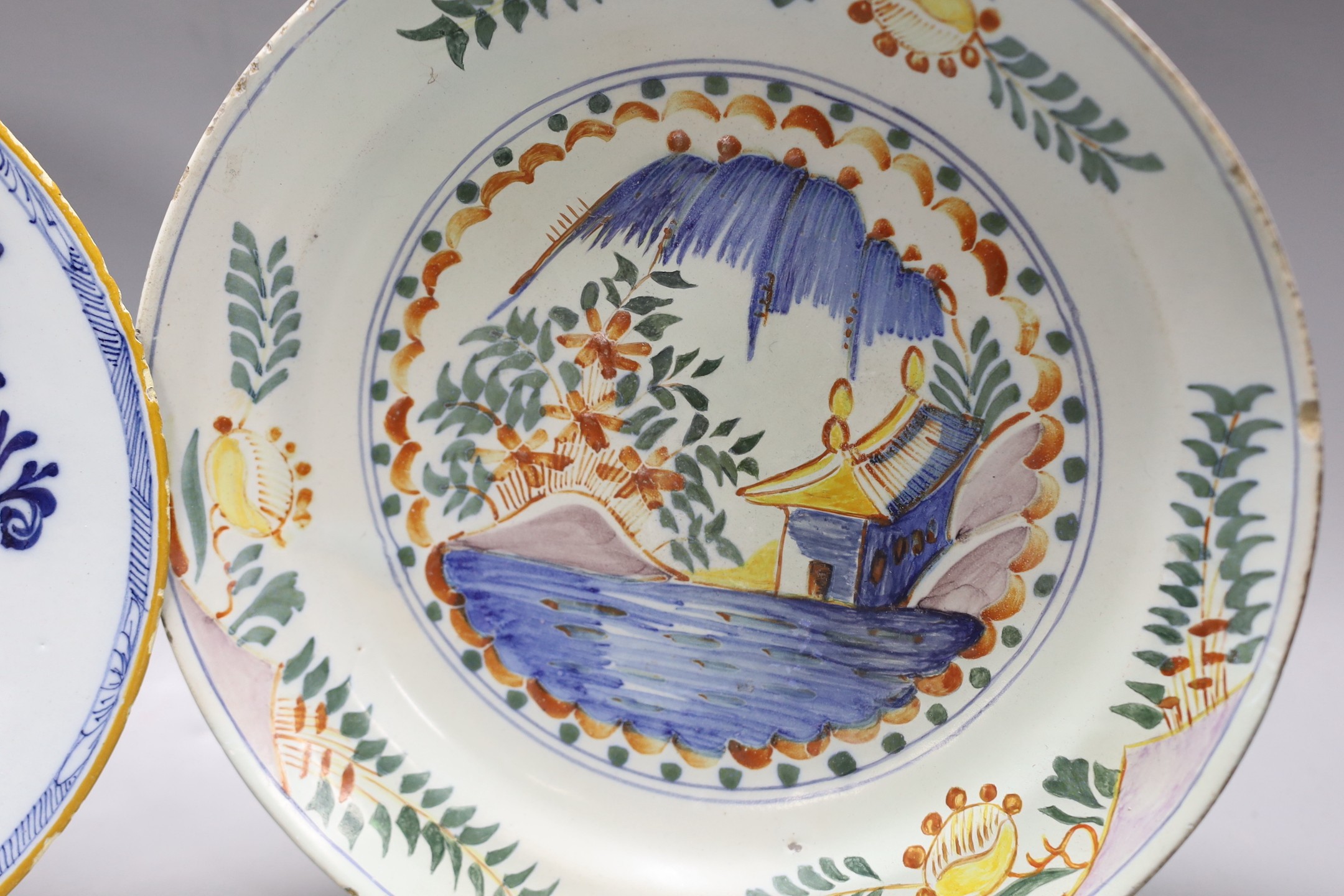 An early 18th century Delft polychrome dish and a mid 18th century Delft blue and white plate, largest 23.5cm diameter